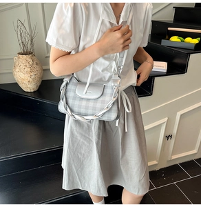 Silver checkered shoulder bag with metallic woven handle shown in a minimalist setting