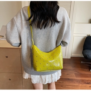 Bright yellow crescent bag with silver rivets shown on a model in a home setting