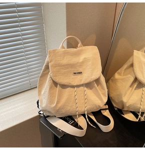 Detail of cream nylon backpack with You Ji Bear logo and woven drawstring on black stand