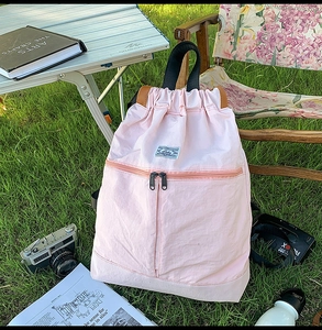 Detailed view of a pink drawstring backpack with dual zipper pockets on a green lawn