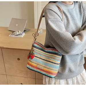 Détail du sac en paille tissé à rayures colorées avec breloques fraises rouges sur l'anse