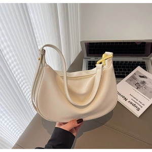 Detail of off-white dumpling bag showing litchi grain texture and gold X-shaped metal buckle