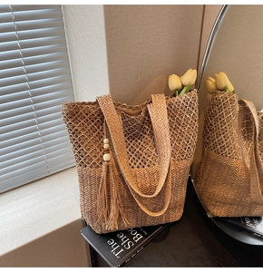 Detail of woven straw tote bag with intricate knit patterns and wooden bead tassel decor