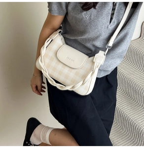 Detail view of beige checkerboard crossbody bag with woven handle and flap closure