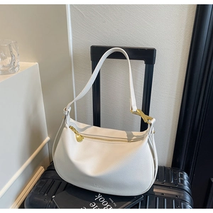 Detail of off-white lychee leather hobo bag with gold zipper on travel suitcase