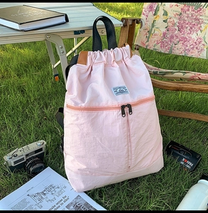Detailed view of a pink drawstring backpack on a sunny lawn with camping accessories