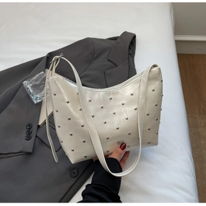 Detailed view of white hobo bag with silver stud accents on a clean white bedding background