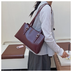 Side view of woman carrying a burgundy patent leather tote bag with silver buckle straps