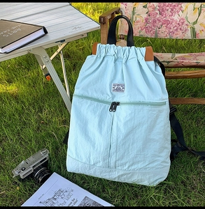 Light blue drawstring backpack on grass with camping gear, featuring large capacity