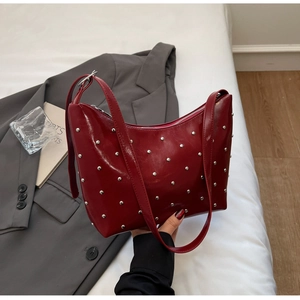 Detail of red glossy leather bag with silver rivets on a stylish grey suit backdrop