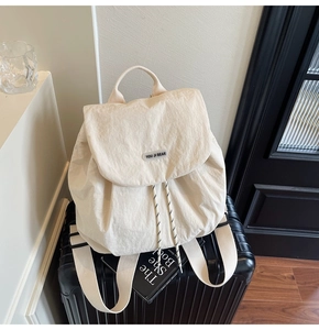 Detail of off-white nylon backpack with drawstring closure on a black suitcase