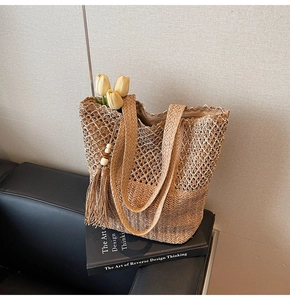 Detail of hand-woven straw tote bag featuring hollow mesh pattern and bead tassels
