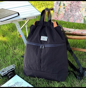 Outdoor lifestyle shot of black drawstring backpack with front zip pocket on grass