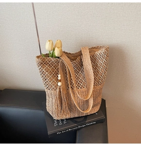 Detail of woven straw tote bag featuring tassel charms and internal lining on a book
