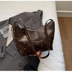 Detail of dark brown patent leather shoulder bag with silver rivet studs and top zipper