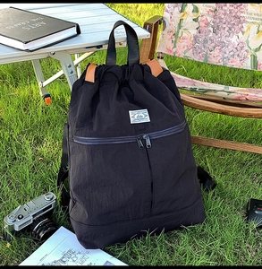 Detail of black nylon drawstring backpack featuring double front zippers on grass