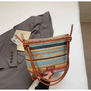 Détail du sac seau tissé coloré avec des breloques fraises rouges et une bandoulière en cuir