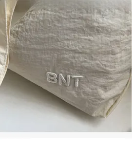 Close-up of white canvas tote bag showing BNT embroidery and wrinkled fabric texture
