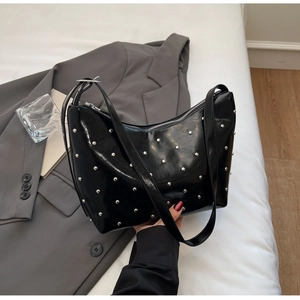 Detail of black patent leather crossbody bag with silver rivet studs and top zipper