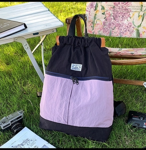 Outdoor scene showing a color-block drawstring backpack on grass with camping gear