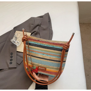 Détail du sac seau tissé avec rayures colorées, bandoulière en cuir et breloques fraises