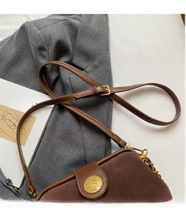 Detail of a dark brown suede crossbody bag with gold metal hardware and a chain strap