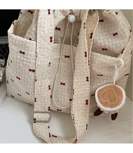 Close-up of beige canvas tote with red bow print, long strap, and heart plush charm