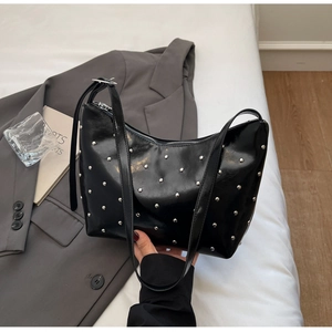 Detail of black glossy patent leather bag featuring silver metal rivets and sleek strap