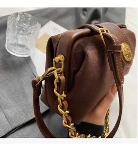 Detailed macro of brown leather and suede bag with gold chain and embossed round buckle