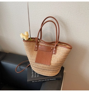 Detail view of woven straw tote bag with brown leather pocket on a black leather sofa