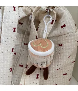 Close-up of a plush coffee cup bag charm with a green heart on a cream backpack