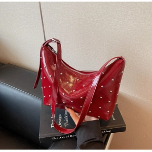 Detail of dark red patent leather hobo bag with silver rivets and adjustable strap