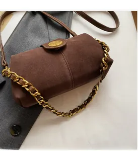 Detail of brown suede doctor bag featuring golden chain and knight emblem on closure