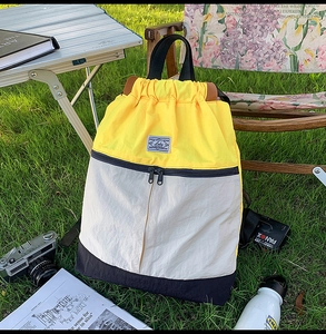 Detail of color-block drawstring backpack with yellow and navy nylon fabric on green grass