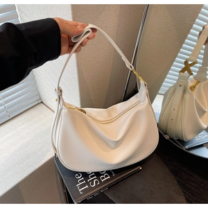 Detailed macro view of white pebble leather texture and gold hardware on a hobo bag