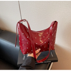 Detail of red patent leather shoulder bag with silver studs and adjustable strap texture