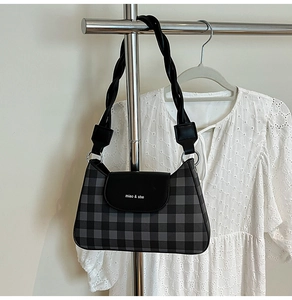 Detail of checkered shoulder bag with woven strap hanging by a white lace dress
