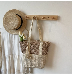 Detailed close-up of woven straw tote bag with floral patterns and tassel charm
