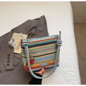Détail d'un sac seau tissé à rayures colorées avec bandoulière en cuir et breloques fraises