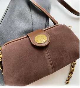 Detail of vintage brown suede crossbody bag with golden metal emblem and leather trim