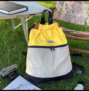 Detail of color-block drawstring backpack with yellow, white and navy panels on grass