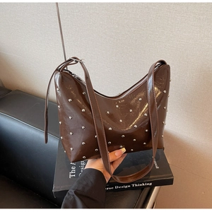 Detail of a brown glossy leather shoulder bag with silver rivets and top zipper closure