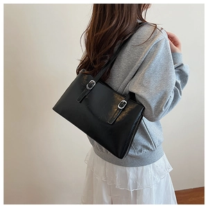 Detail of glossy black leather tote bag featuring adjustable silver metal buckles and straps