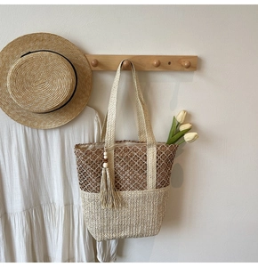 Detail of handwoven large capacity straw tote bag with bicolor texture and tassels