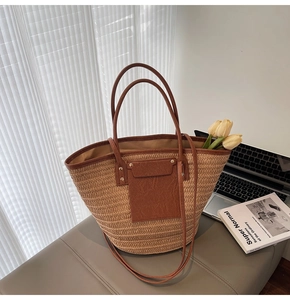 Close-up of woven straw tote bag featuring brown faux leather handles and metal rivets