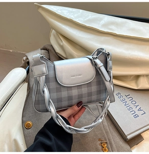 Detail of silver checkered crossbody bag with thick woven shoulder strap and metal texture
