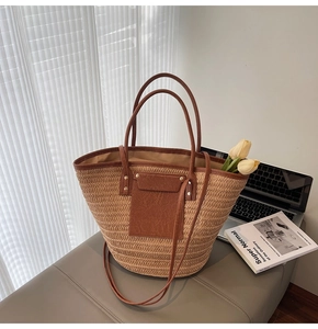 Detail of woven straw tote bag with brown leather trim and handles near tulip decor