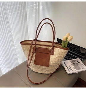 Detail of woven straw tote bag with brown trim and front pocket in indoor setting