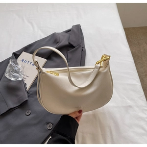 Detail view of cream lychee-grain leather shoulder bag with golden zipper on white fabric