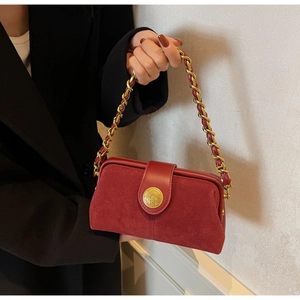 Detail of red suede doctor bag with gold emblem and woven chain shoulder strap